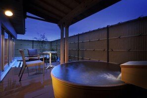 An outdoor hot tub area with a wooden deck, a seating area with a table and chairs, and a bamboo fence in the background. - Kami No Yama Azumaya (Kaminoyama)