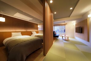 Quarto de hotel com duas camas, uma mesinha, televisão e um separador deslizante.