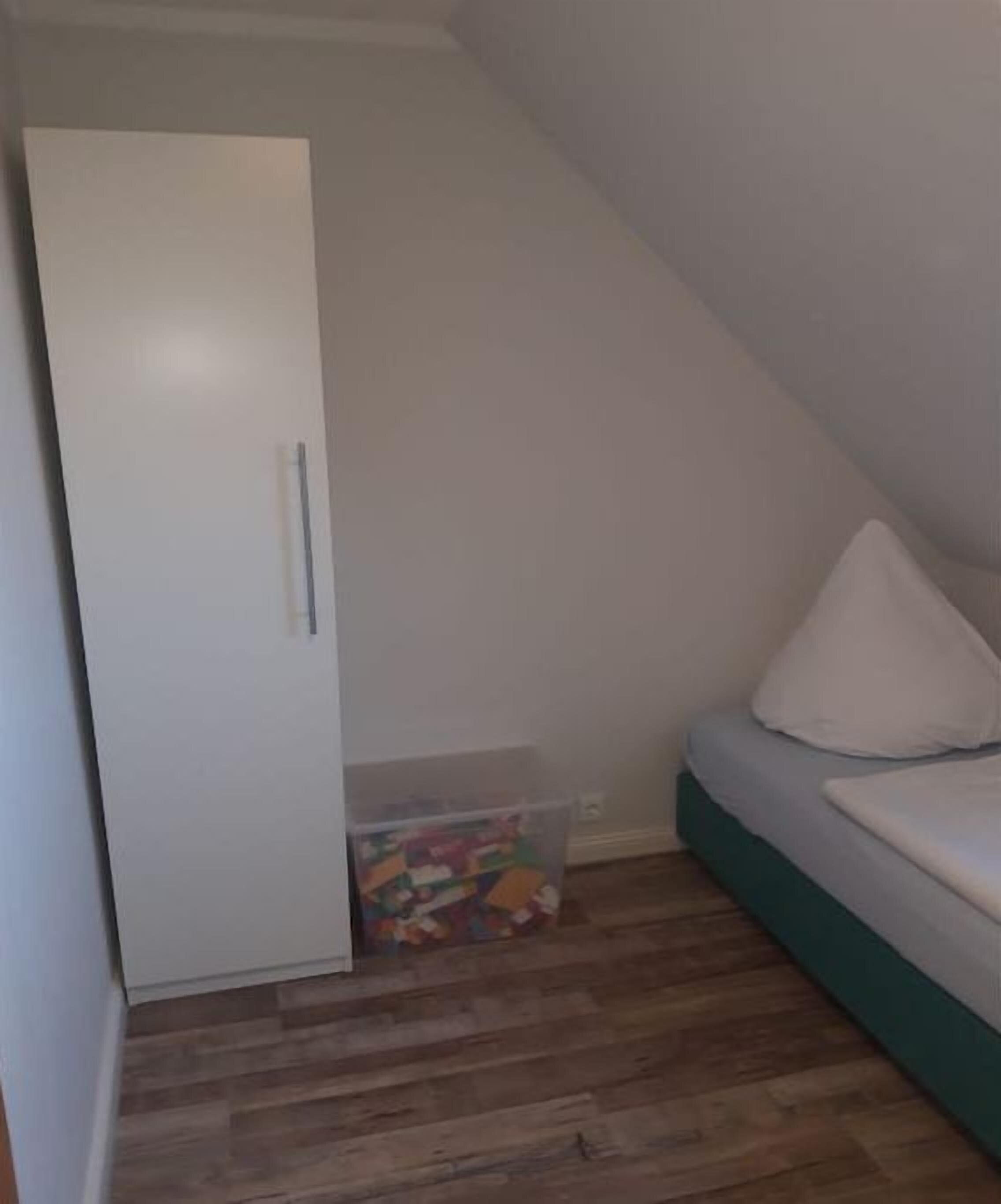 Une chambre à coucher avec un lit, une armoire blanche et une boîte de rangement contenant des jouets.