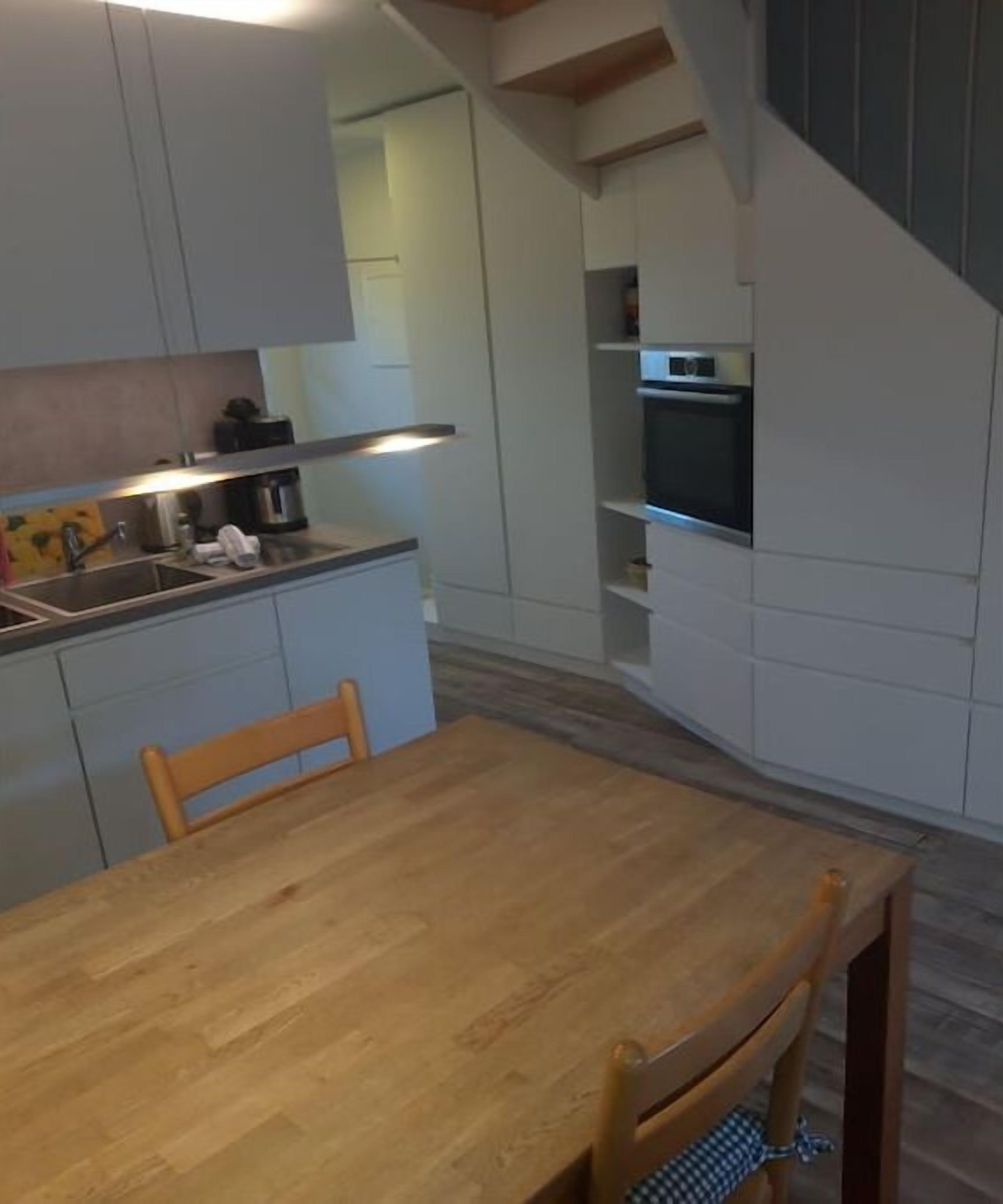 A compact kitchen with white cabinetry, a wooden dining table, and a built-in oven.