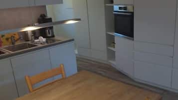 A compact kitchen with white cabinetry, a wooden dining table, and a built-in oven.