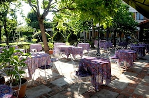 An outdoor patio with multiple round tables and chairs, surrounded by trees and a garden. - Hotel Le Dahu (Parigny)