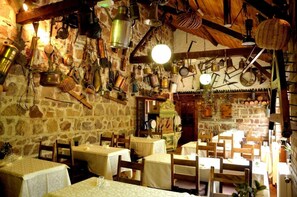 A rustic dining area with stone walls, wooden beams, and tables set for dining. - Hotel Le Dahu (Parigny)