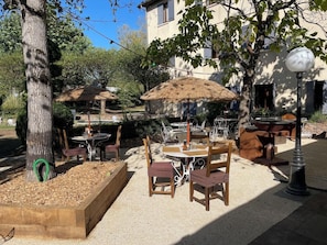 An outdoor seating area with tables and chairs, surrounded by trees and a building in the background. - Hotel Le Dahu (Parigny)