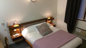 A neatly made bed with a white comforter and a purple throw blanket, flanked by two bedside tables with lamps. - Hotel Le Dahu (Parigny)