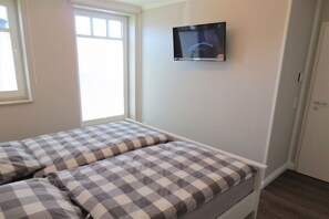 A bedroom with a bed, a television mounted on the wall, and a window. - Holiday apartment with 2 bedrooms (Börgerende)