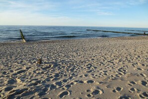 Ein Sandstrand mit Fußspuren, ein hölzerner Steg und ruhiges Wasser.