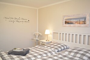 Ein Schlafzimmer mit kariertem Bettbezug, einer Nachttischlampe, einem gerahmten Bild an der Wand und einer dekorativen Wandsticker.