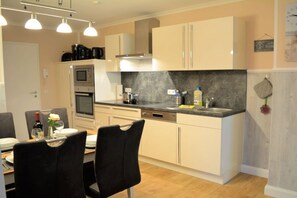 A modern kitchen with a built-in oven, microwave, and coffee maker. There is a dining area with a table set for two. - Holiday apartment with 2 bedrooms (Börgerende)
