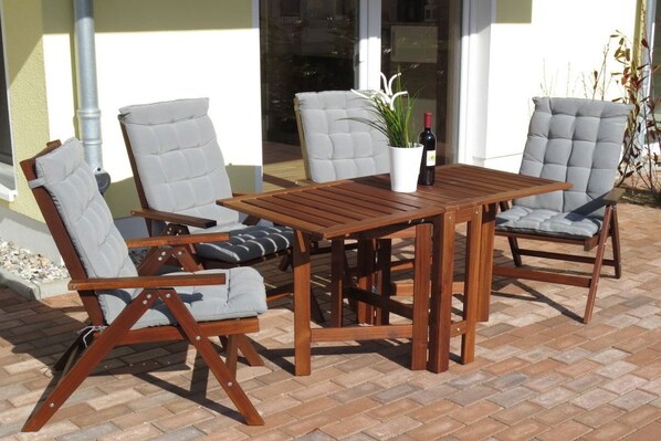 Een terras buiten met een houten tafel en vier stoelen met kussens.
