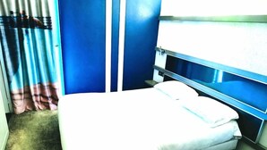 Ein Einzelbett mit weißer Matratze und Kissen, eine blaue Wand und ein Fenster mit Vorhängen.
