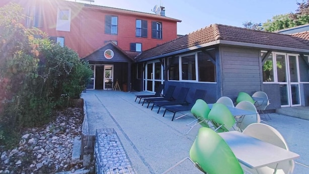 Ein Gebäude mit roter Fassade, eine überdachte Außenbereich-Sitzgelegenheit mit Stühlen und Tischen sowie einem klaren Himmel.