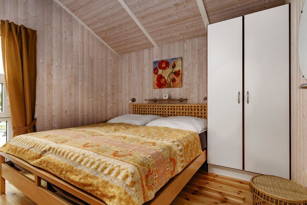 A wooden-paneled room with a bed, a wardrobe, and a painting on the wall.
