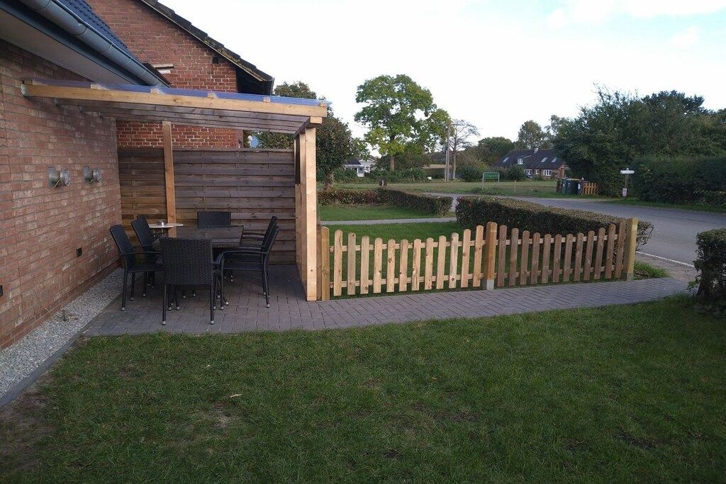 Een terras met houten omheining, bakstenen muur en gazon.