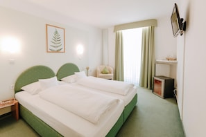 Een hotelkamer met een tweepersoonsbed, een stoel, een bureau met een computer en een televisie aan de muur.