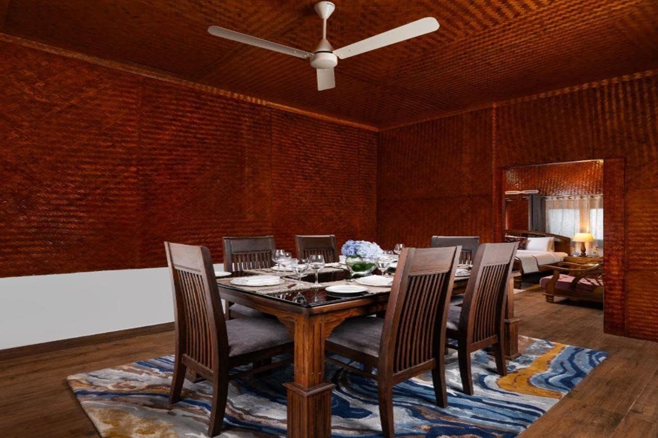 A dining room with a brick wall, a ceiling fan, a dining table set for six, and a patterned rug.