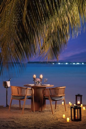 A beachside dining setup with a table, chairs, candles, and a lantern. - Bangaram Island - Ihcl Seleqtions (Bangaram Island)
