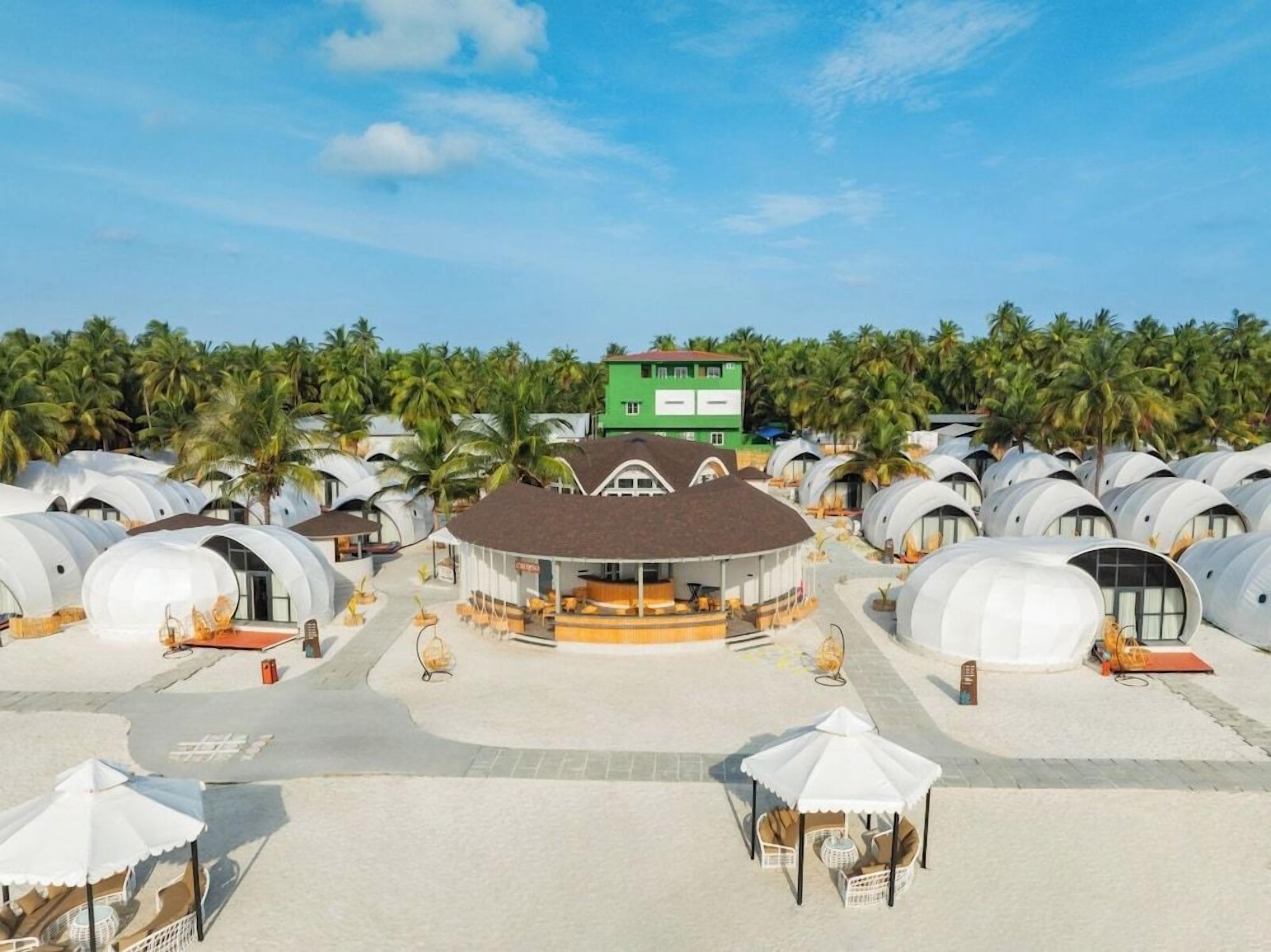 A resort with dome-shaped accommodations, a central building, and a palm tree-lined background.