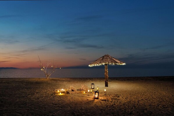 Escena de playa al anochecer con un solo paraguas y faroles.