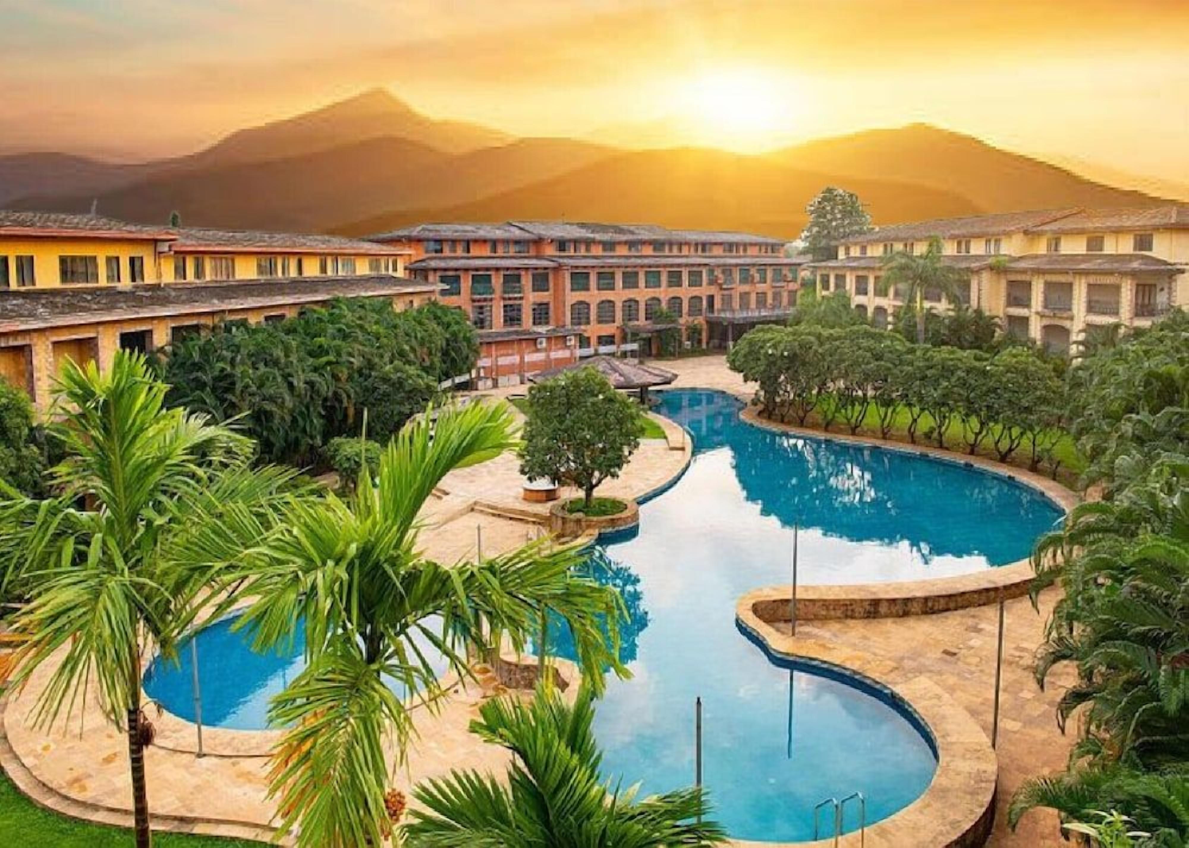 Resort com área de piscina cercada por palmeiras e montanhas ao fundo.