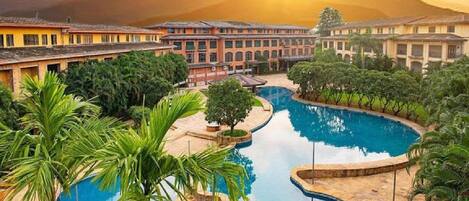 Resort com área de piscina cercada por palmeiras e montanhas ao fundo.