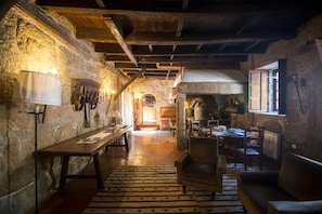Un interior rústico con paredes de piedra, techo de madera, zona de comedor con sillas y mesa, y alfombra estampada.
