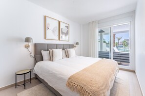 A hotel room with a large bed, two wall-mounted lamps, a small side table, and a view of a pool and buildings through a sliding glass door. - AMPHORA BEACH RESIDENCE 2476 MANILVA (Manilva)