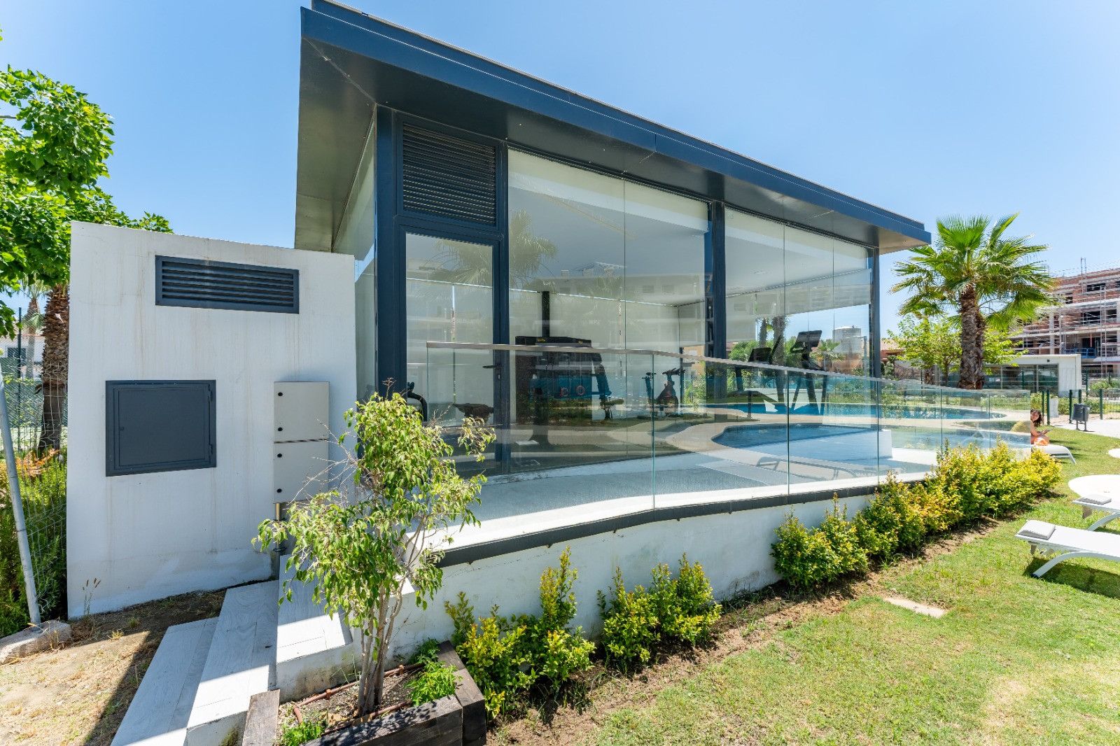A modern building with a glass facade, a pool, and a well-maintained garden.
