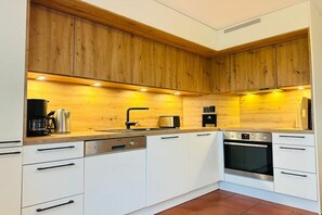 A modern kitchen with wooden cabinets, a dishwasher, an oven, and a coffee maker. - Holiday apartment with 2 bedrooms (St. Peter - Ording)