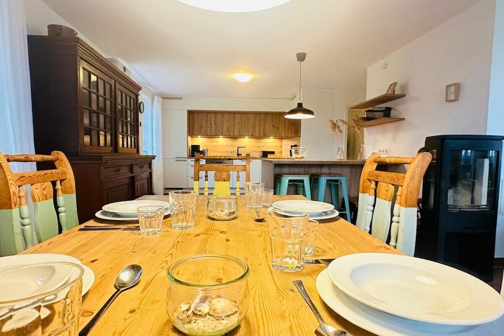 Une table à manger mise pour quatre personnes, avec des chaises, un buffet en bois et une cuisine en arrière-plan.