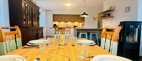 Una mesa de comedor preparada para cuatro personas, con sillas, un armario de madera y una cocina al fondo.