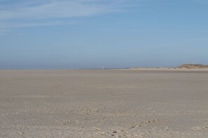 Ein breiter, flacher Sandstrand mit einem fernen Leuchtturm.