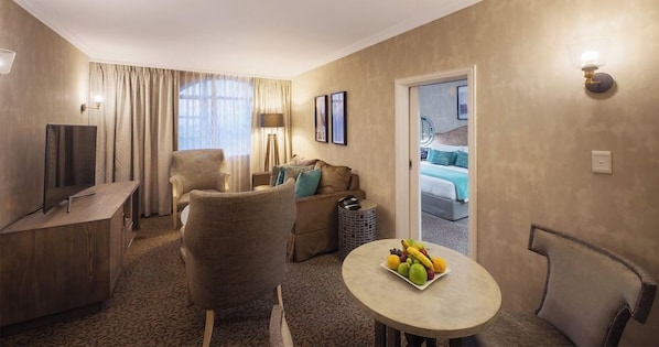 A hotel room with a television, seating area, and a dining table with fruit.