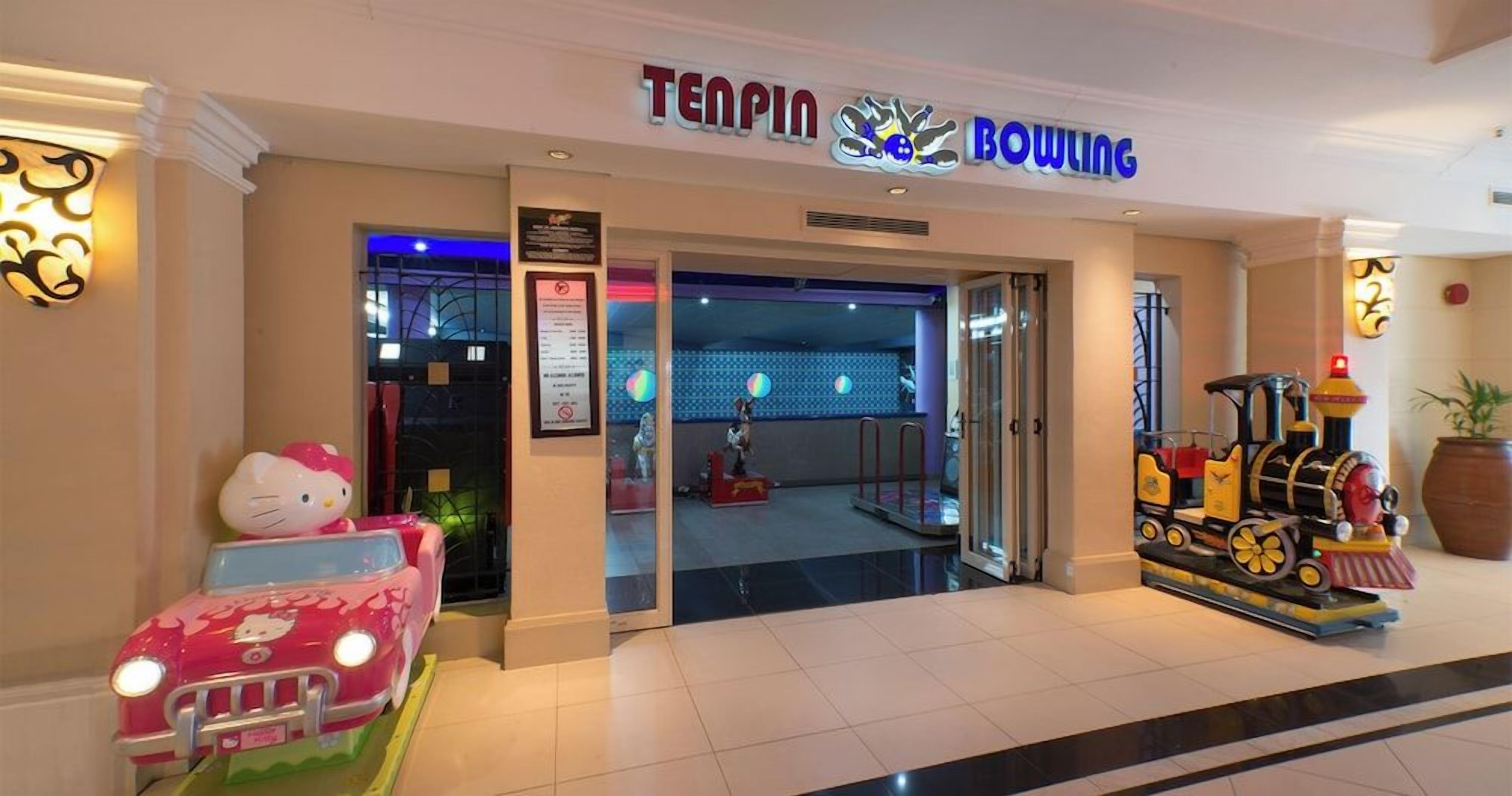 A bowling alley entrance with a neon sign, a Hello Kitty car, and a toy train.