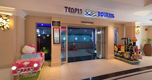 A bowling alley entrance with a neon sign, a Hello Kitty car, and a toy train.