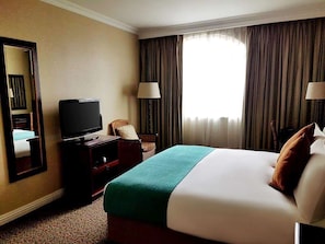 A hotel room with a bed, a television, a chair, and a window with curtains.