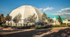A large, white, dome-shaped building with a green roof, surrounded by trees and a paved area.