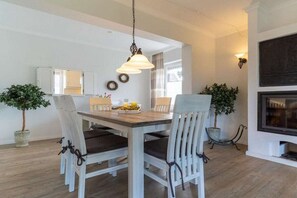 En matplats med ett träbord och stolar, en hängande lampa och krukväxter.