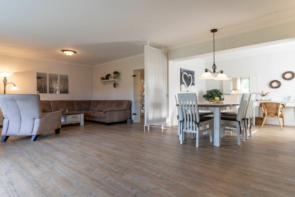 A modern living room with a sectional sofa, a dining area with a table and chairs, and a kitchen in the background.