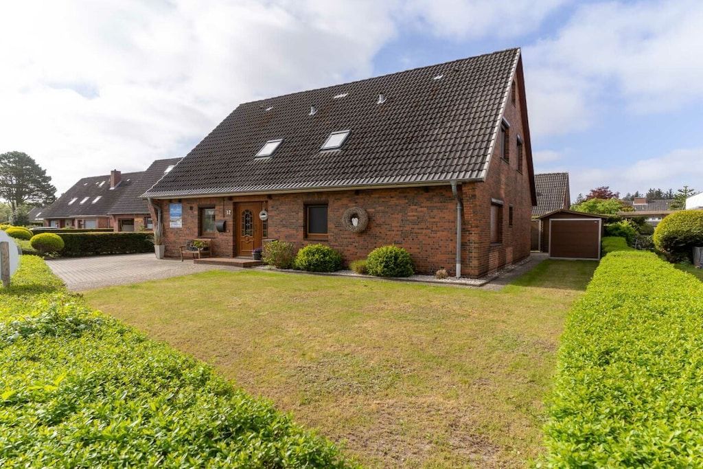 A brick house with a sloped roof, a front door, and a small front yard with hedges.
