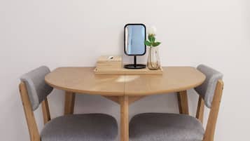 A round wooden table with two grey upholstered chairs, a small vase with a white flower, and a framed picture on the wall.