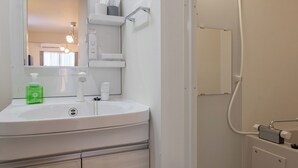 A modern bathroom with a white sink, mirror, and a shower area. - SunLight Kishinosato (Tamade-naka, Nishinari-ku)