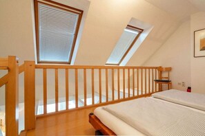 Un dormitorio con techo inclinado, barandilla de madera y una cama con colchón blanco.