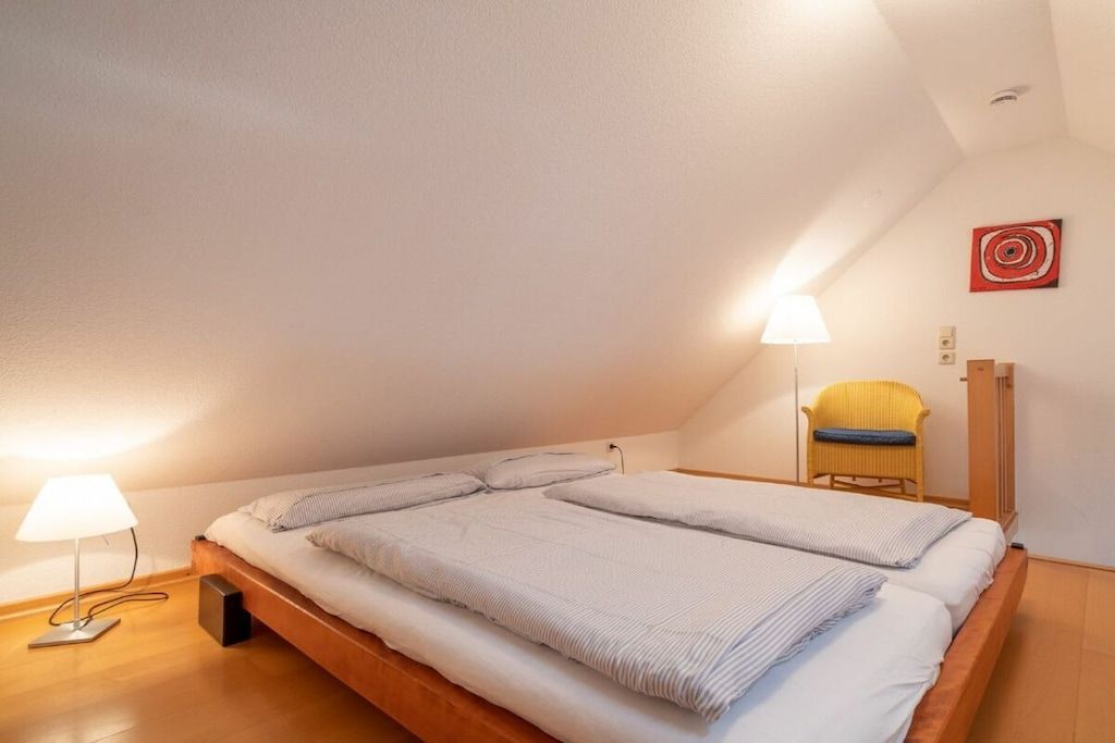 Een slaapkamer met een groot bed, twee bedlampen, een stoel en een kunstwerk aan de muur.