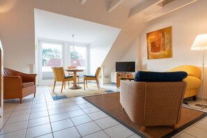 Una sala de estar moderna con un sofá, una mesa de comedor con sillas, un televisor y un cuadro en la pared.