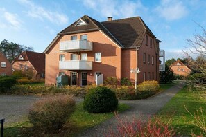 A two-story brick building with a balcony, a covered entrance, and a well-maintained garden. - Holiday apartment with 2 bedrooms (St. Peter-Ording)