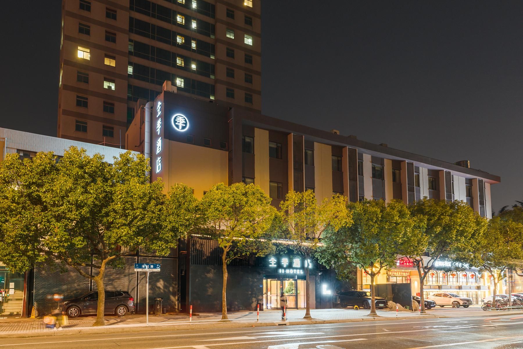 A hotel with a prominent sign, a modern building facade, and a street view with parked cars and trees.