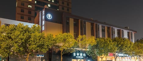 A hotel with a prominent sign, a modern building facade, and a street view with parked cars and trees.