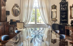 Una habitación con una mesa de vidrio, dos sillas, un ventanal con cortinas y varios objetos decorativos.