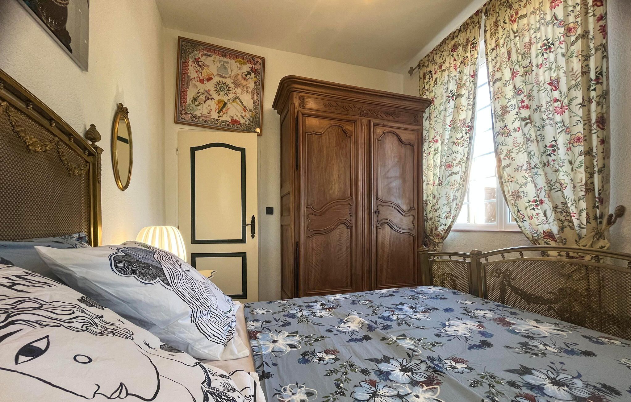 A bedroom with a bed, a wardrobe, a mirror, and a floral curtain.